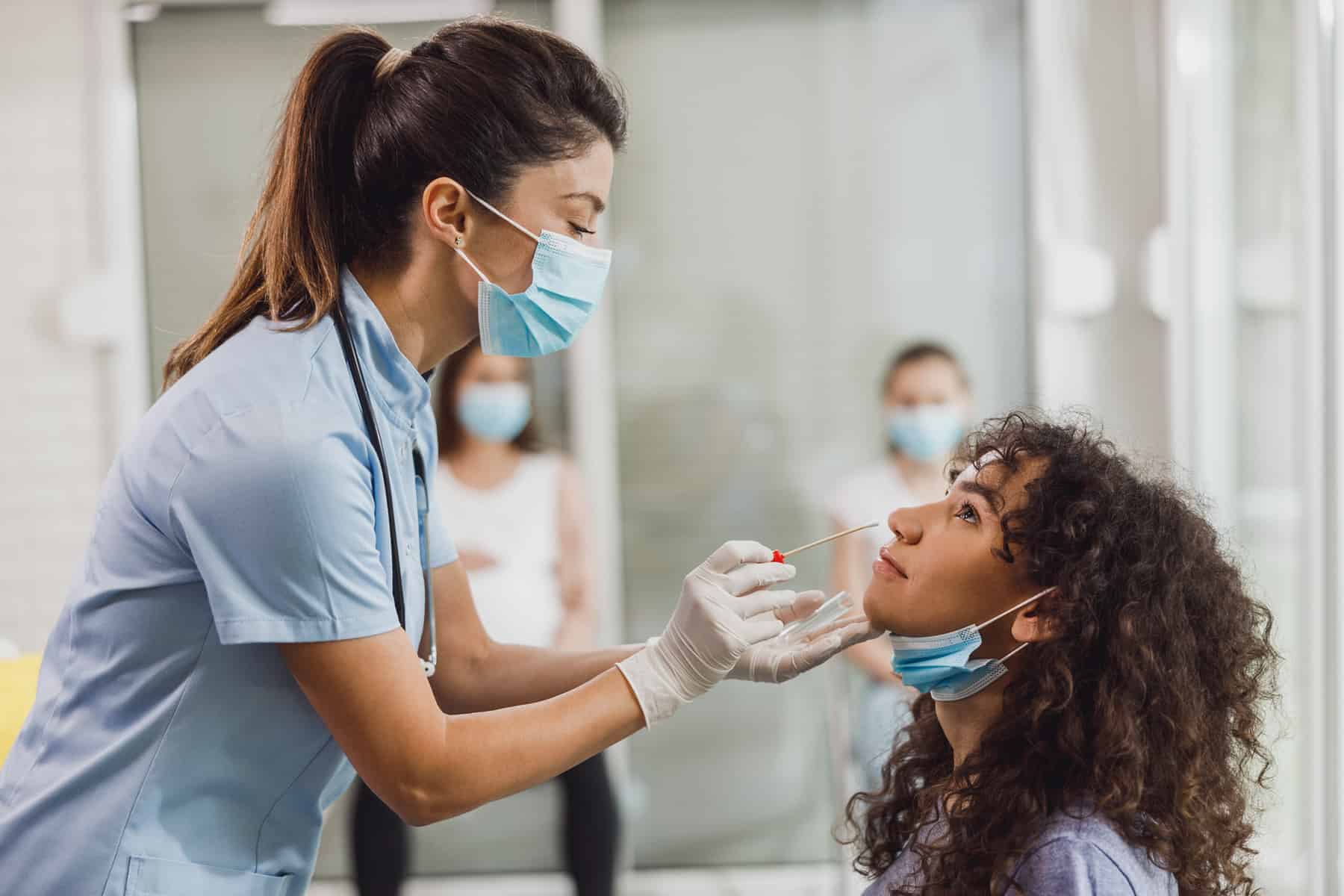 Une infirmière approche un écouvillon du nez d'une jeune femme aux cheveux bouclés