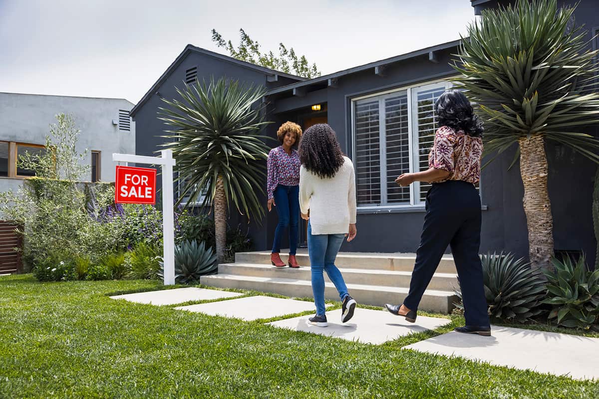 Une femme agent immobilier noire accueille deux femmes noires devant une maison à vendre