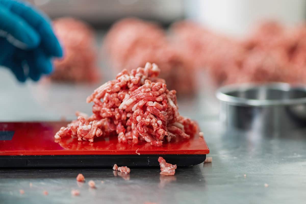Main gantée d'une personne pesant de la viande hachée