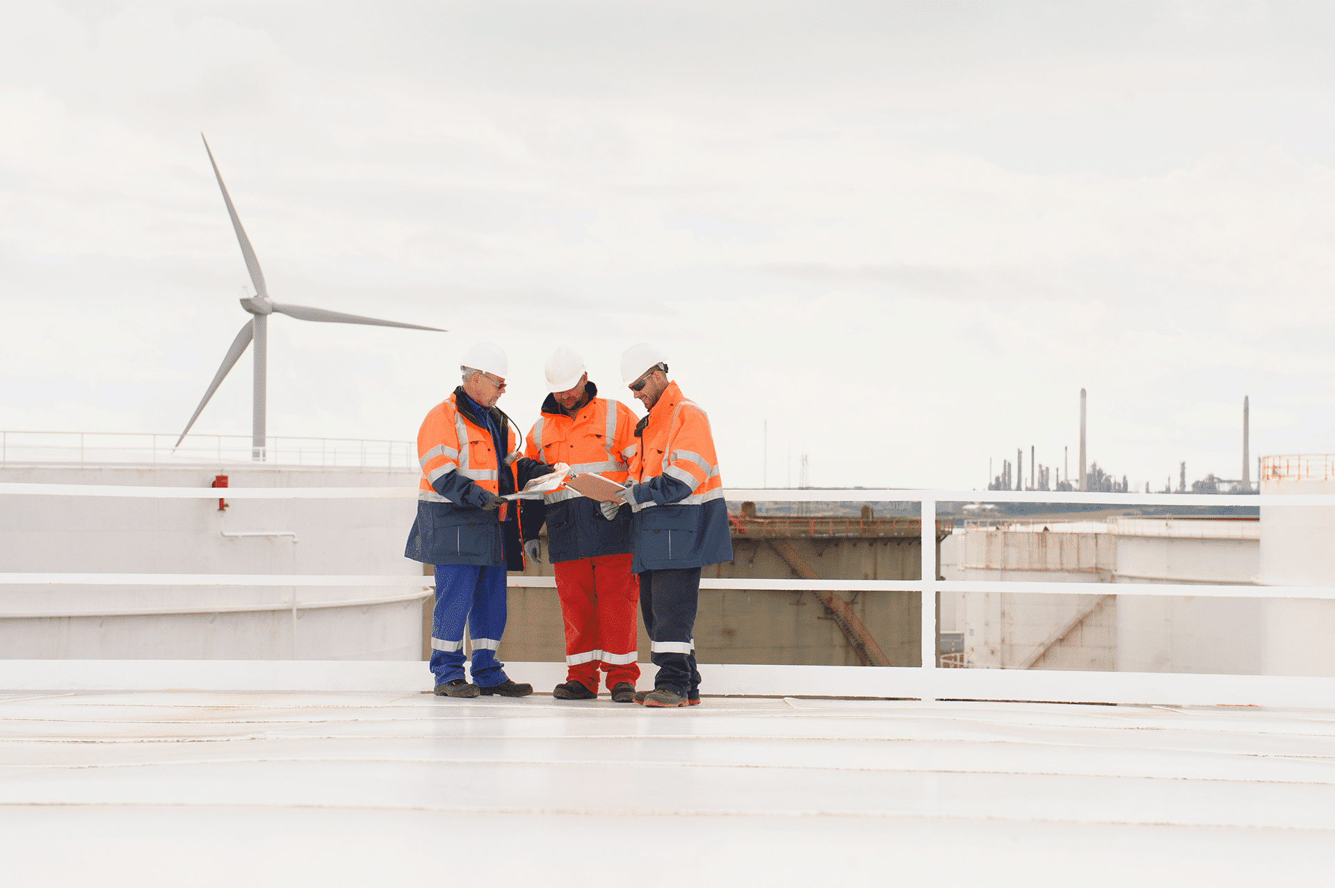 Trois hommes blancs en vêtements de chantier sur le toit d'un bâtiment faisant face à une éolienne