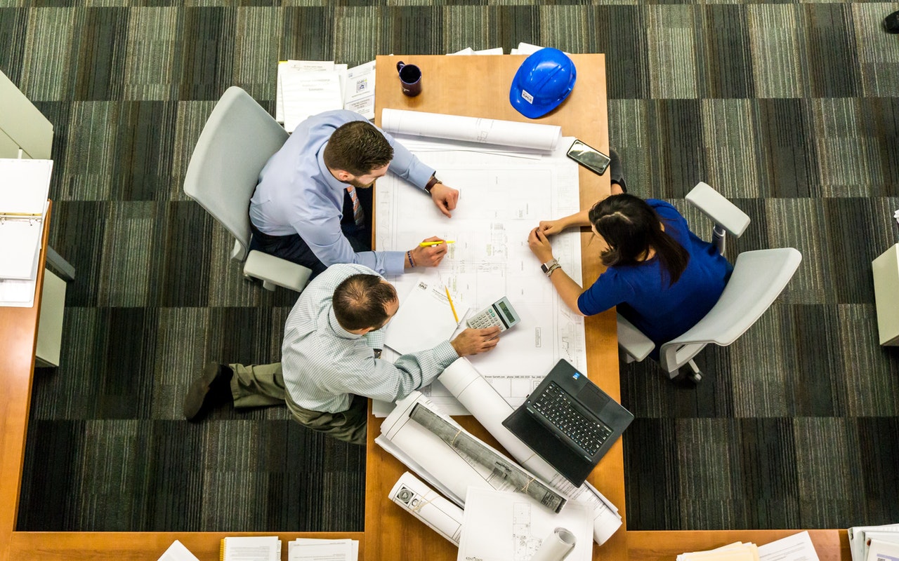 Aerial view of three people around a table on which plans are laid