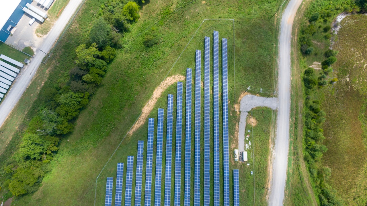 Vue en plongée de panneaux solaires dans une prairie à droite de bâtiments logistiques