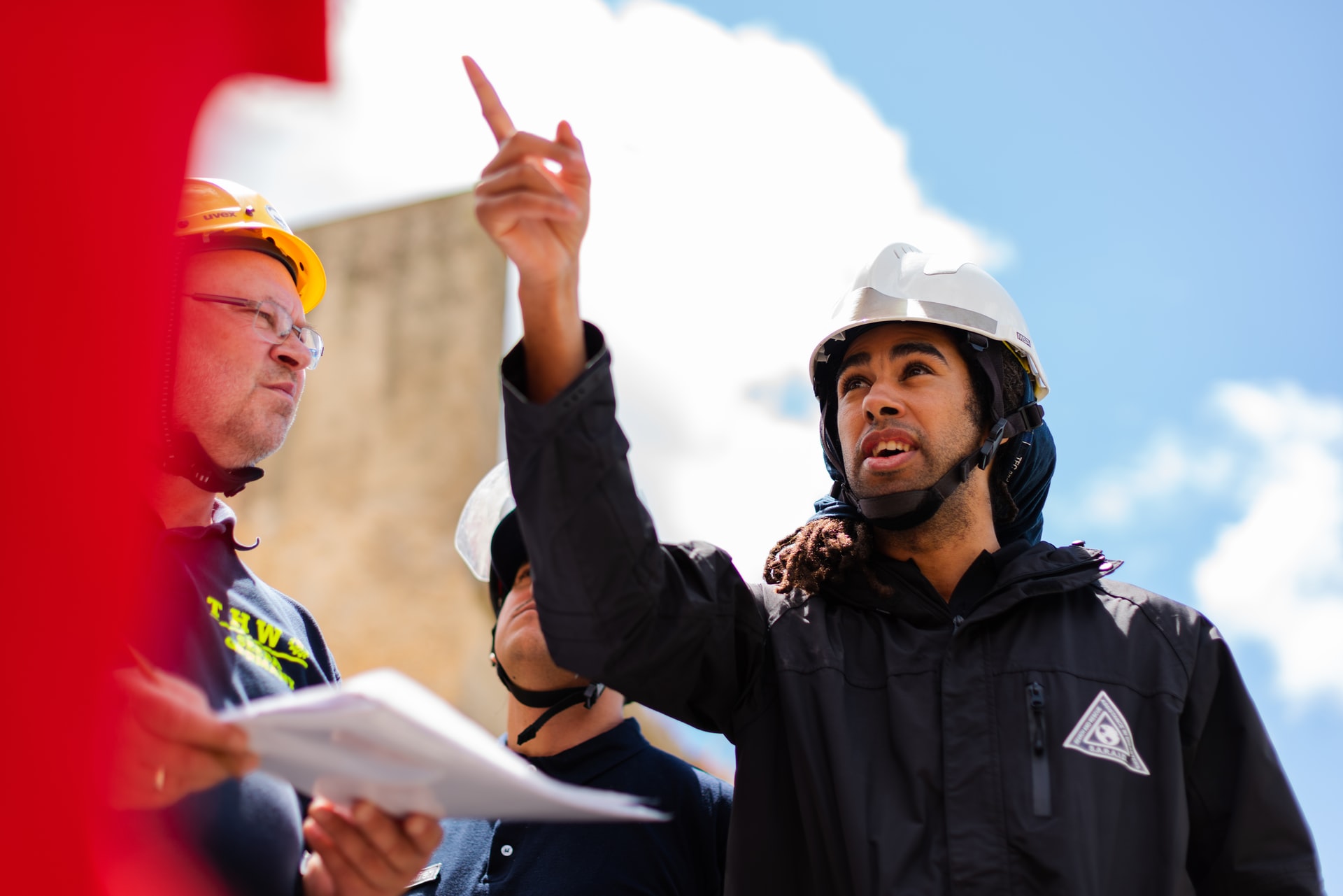 Trois hommes en casque de chantier l'un pointe l'air du doigt