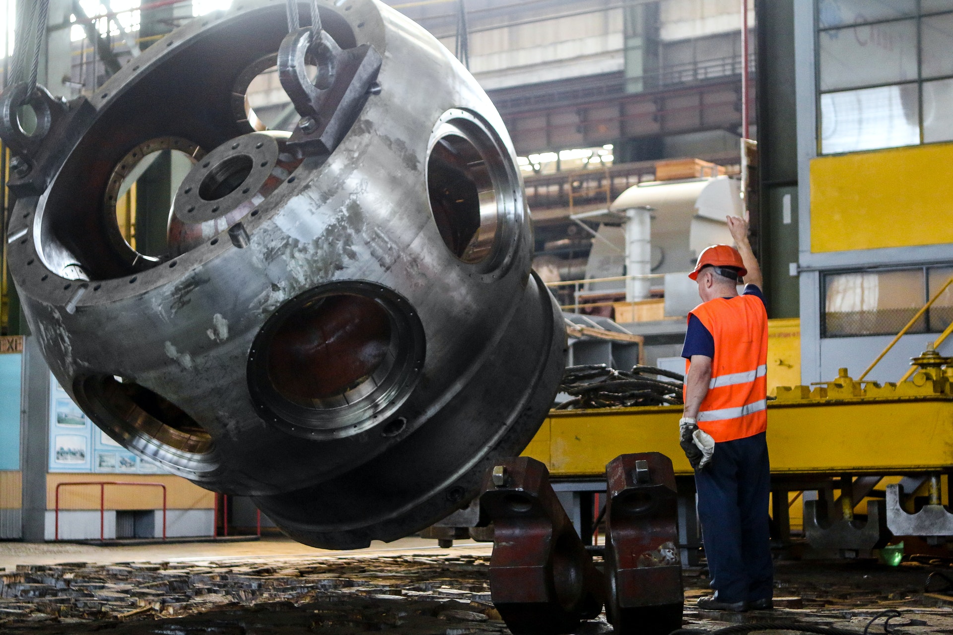 Un homme vêtu d'un gilet et d'un casque orange à côté d'une pièce métallique industrielle