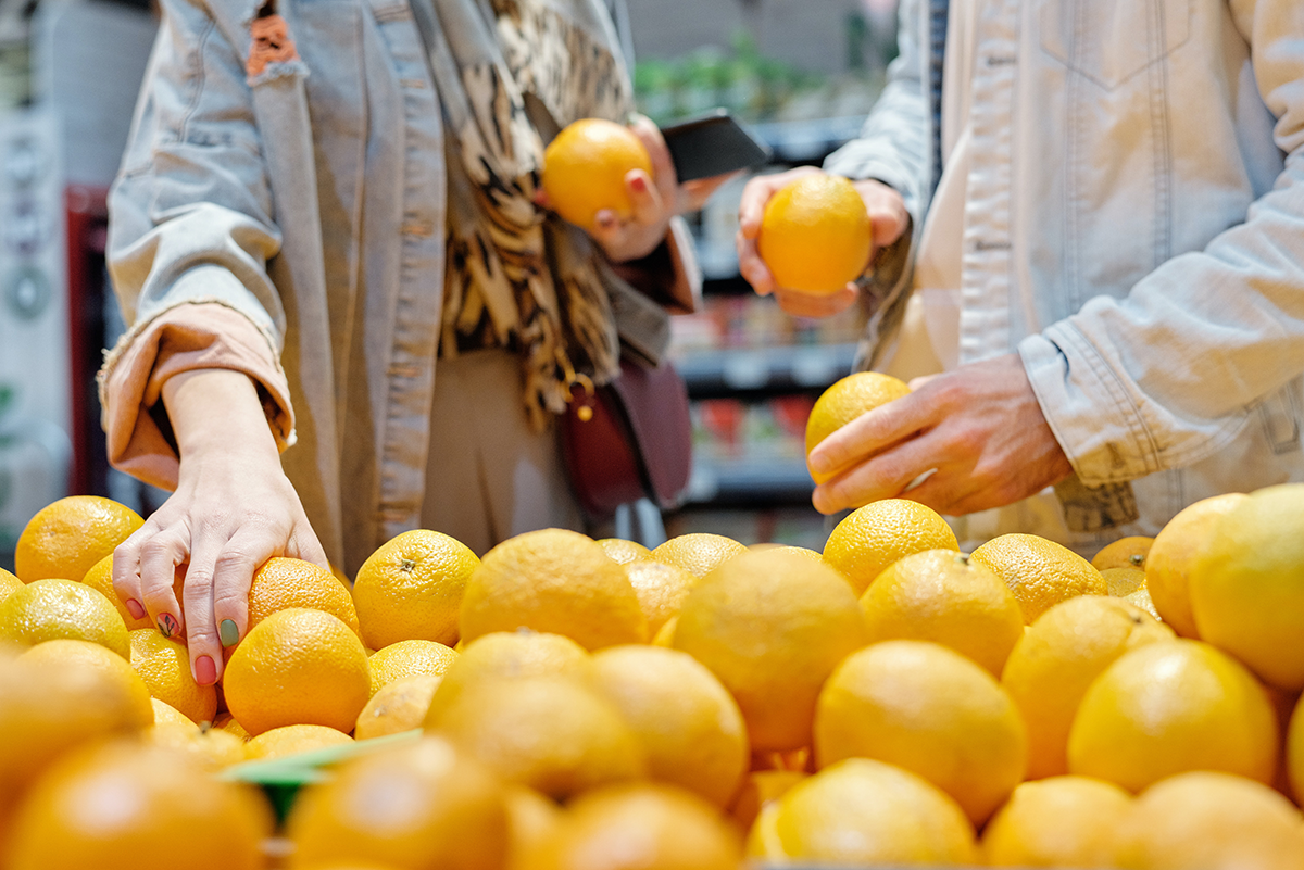 Plan rapproché des mains de deux personnes blanches saisissant des oranges dans une supermarché