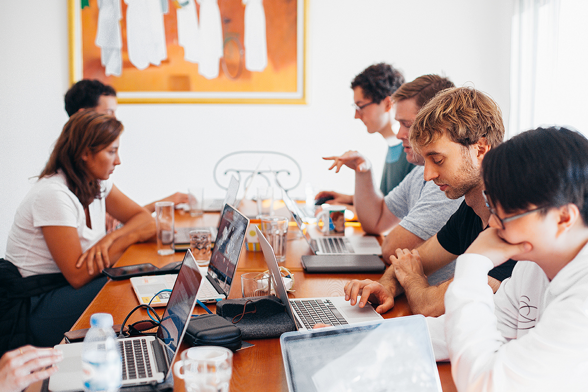 Six personnes assises autour d'une table rectangulaire travaillent sur leurs ordinateurs