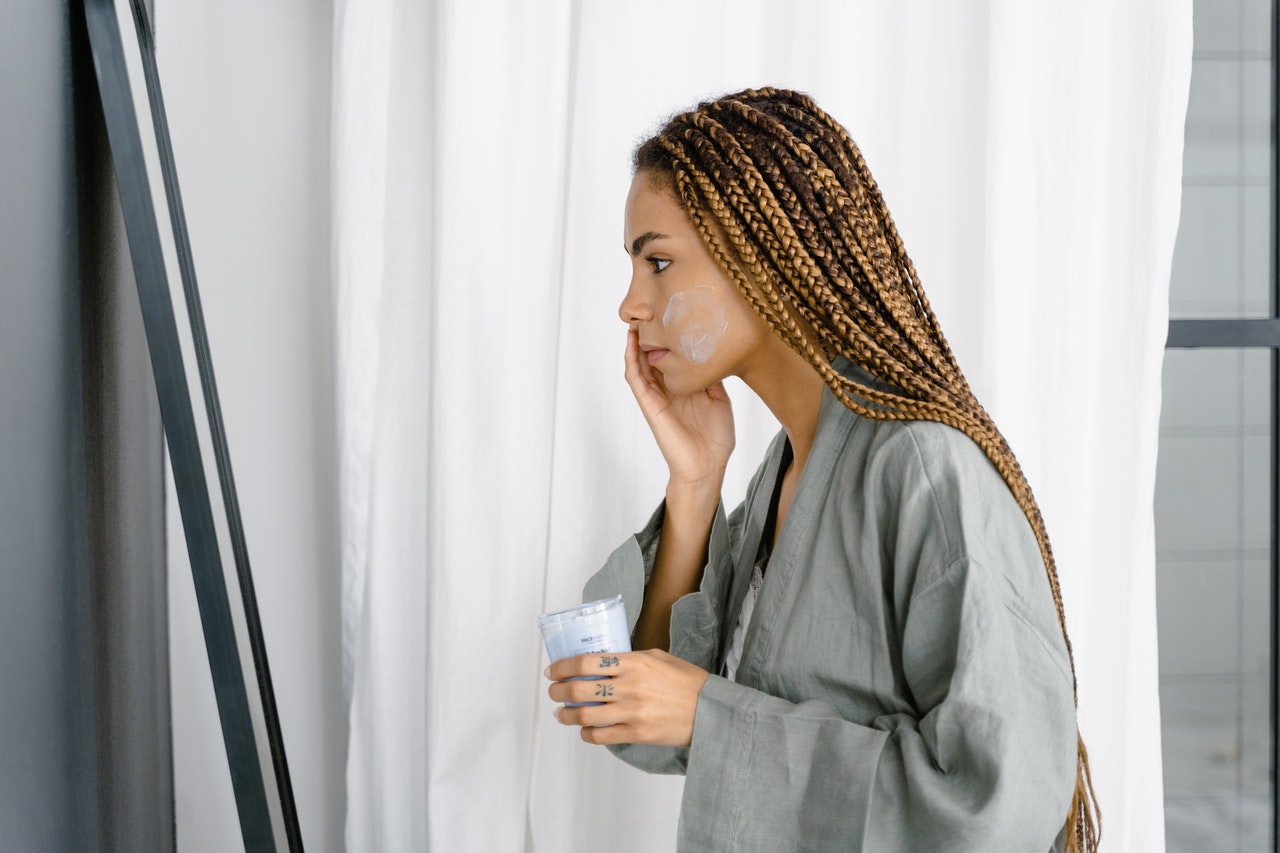 Une femme à la peau mate et aux cheveux tressés applique de la crème sur son visage