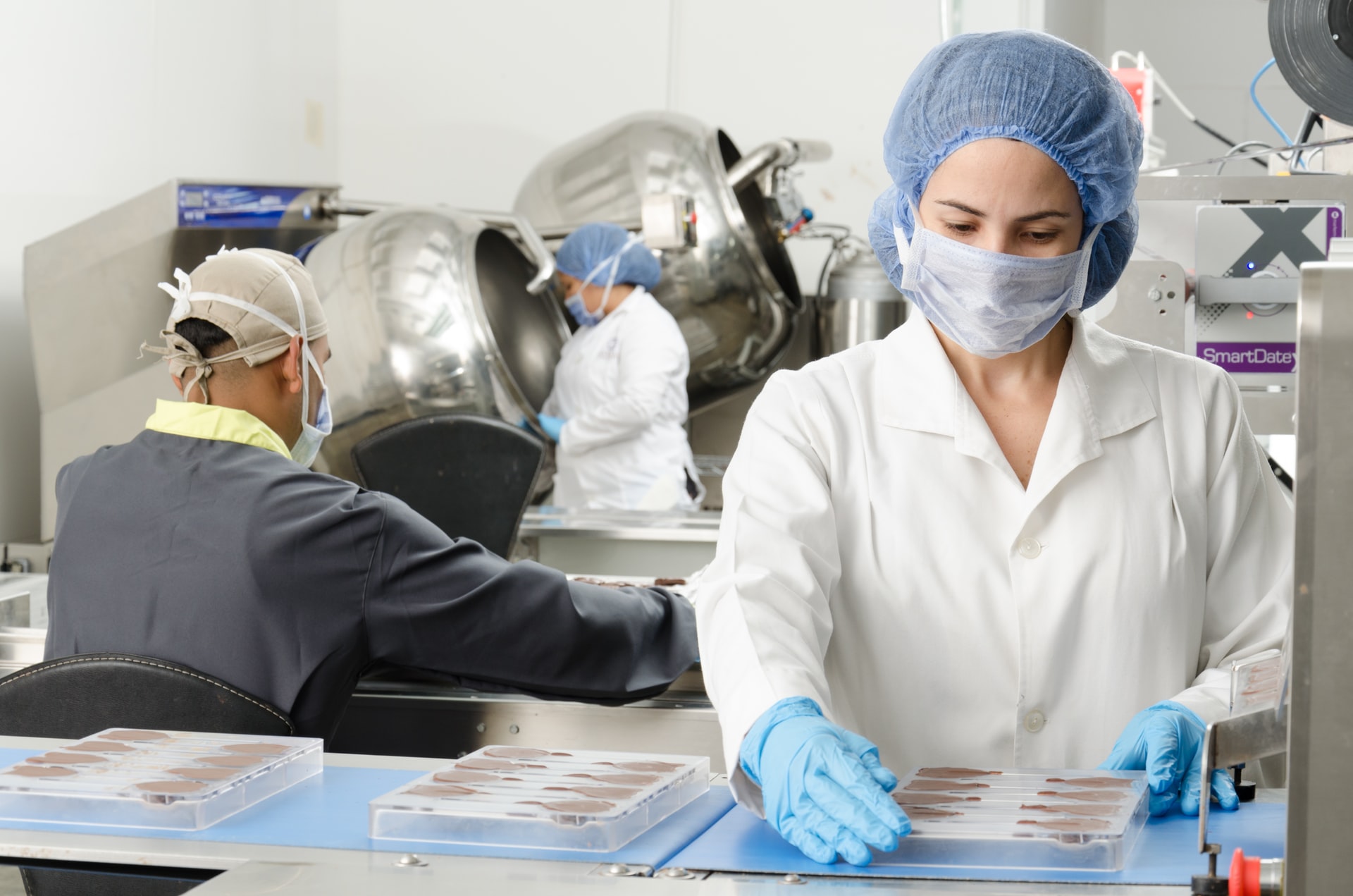 Personne blanche portant une blouse, un masque, une charlotte et des gants dans une usine agroalimentaire