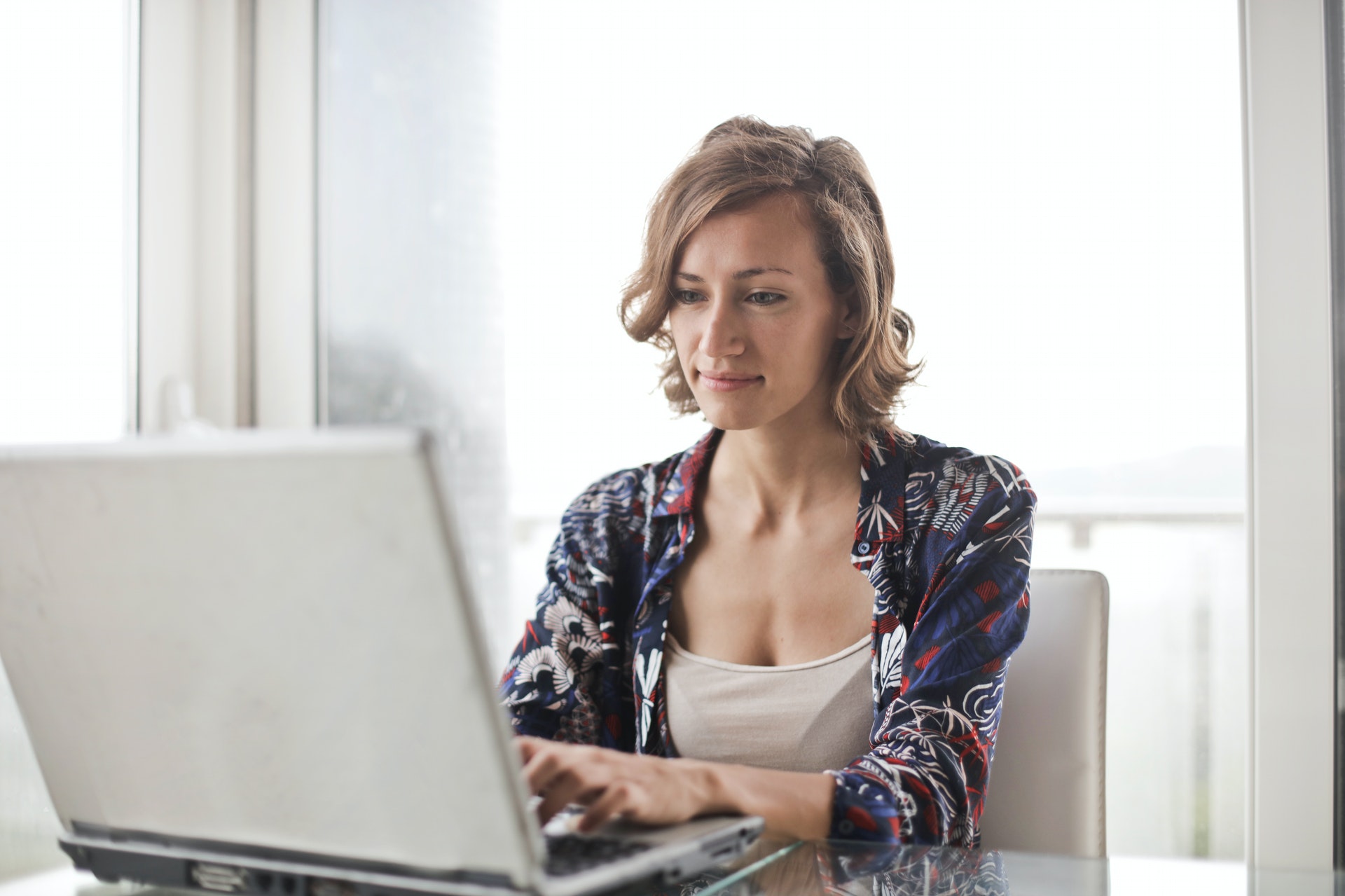 Une femme blanche assise à un bureau travaille sur son ordinateur portable