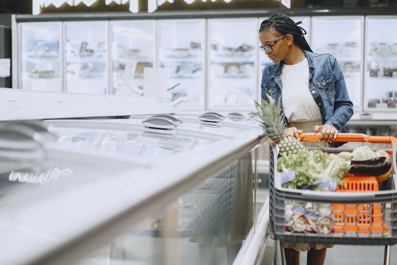 Une femme noire dans un supermarché regarde les meubles de surgélation