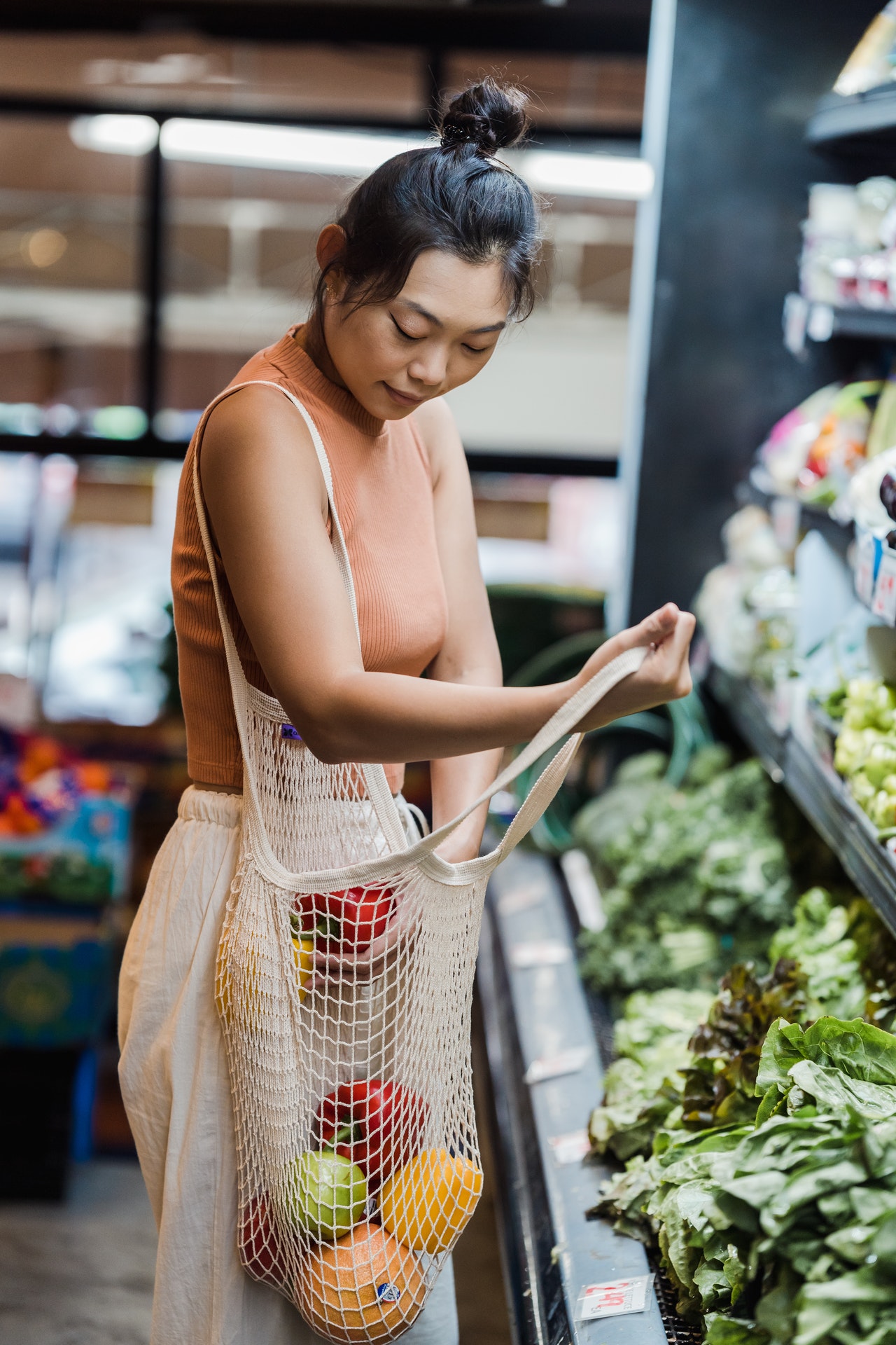 Dans un supermarché une femme asiatique dépose un légume dans son sac en filet