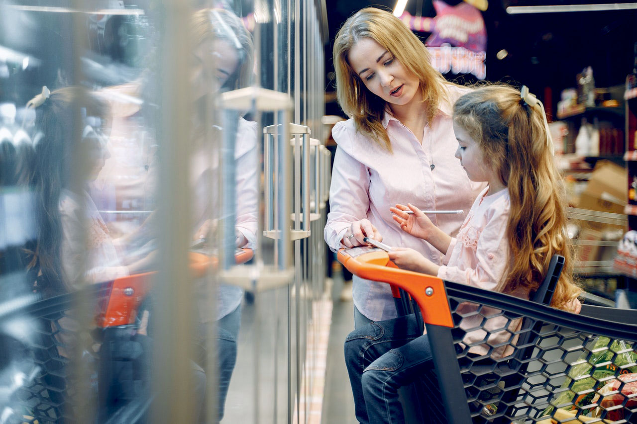 Une fillette assise dans un chariot de supermarché écrit sur une liste près d'une femme debout à côté d'elle