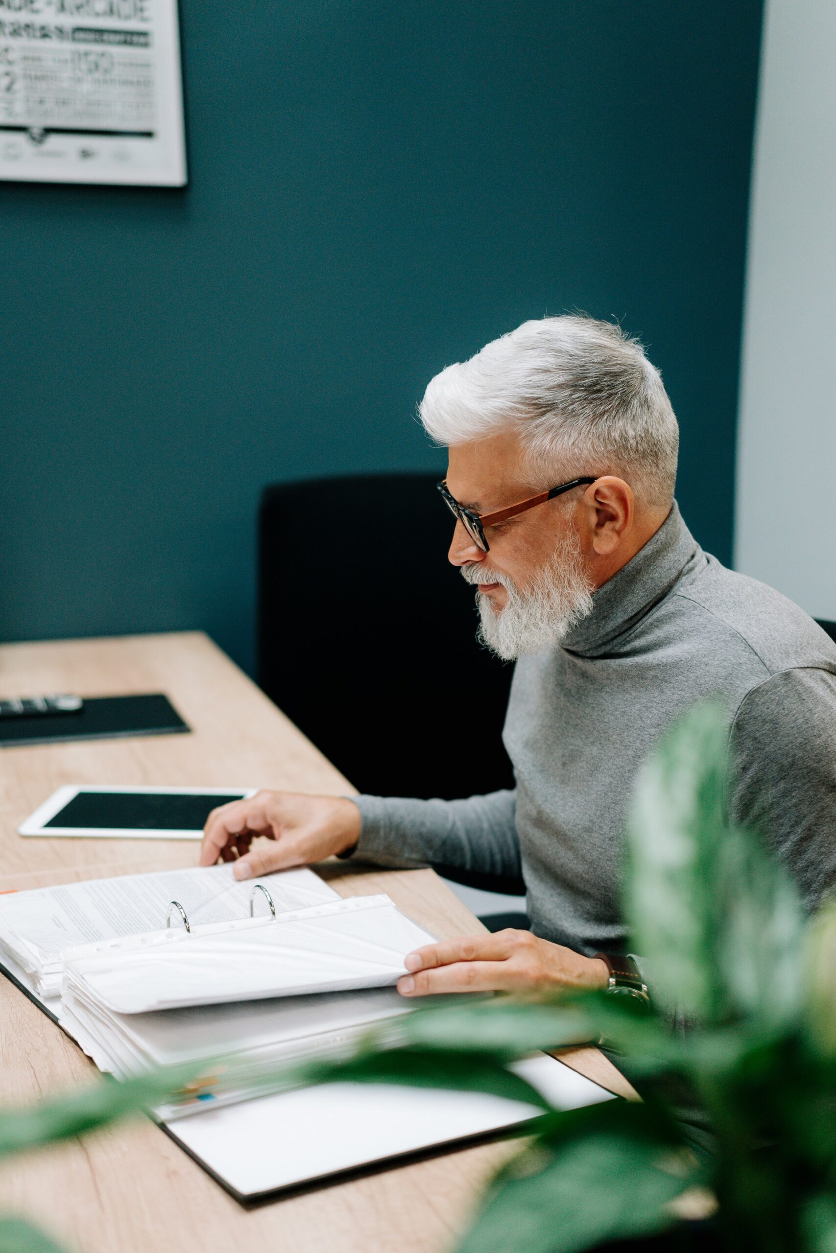 Un homme aux cheveux et à la barbe blancs lit un document assis à un bureau