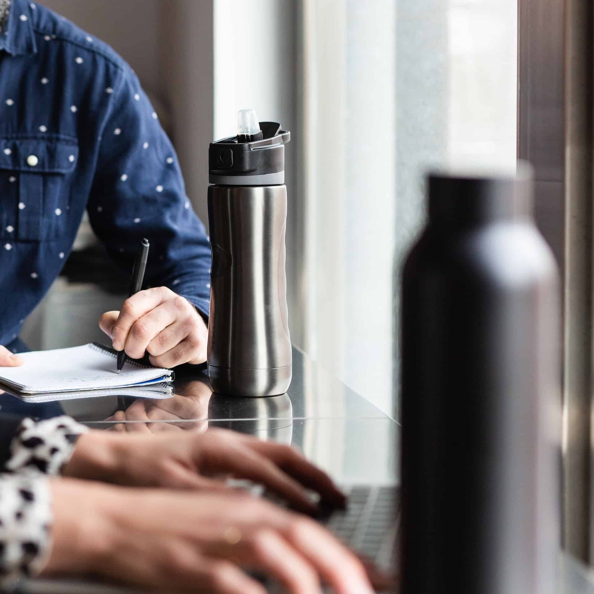 Deux gourdes posées sur une table à côté des mains de personnes qui écrivent