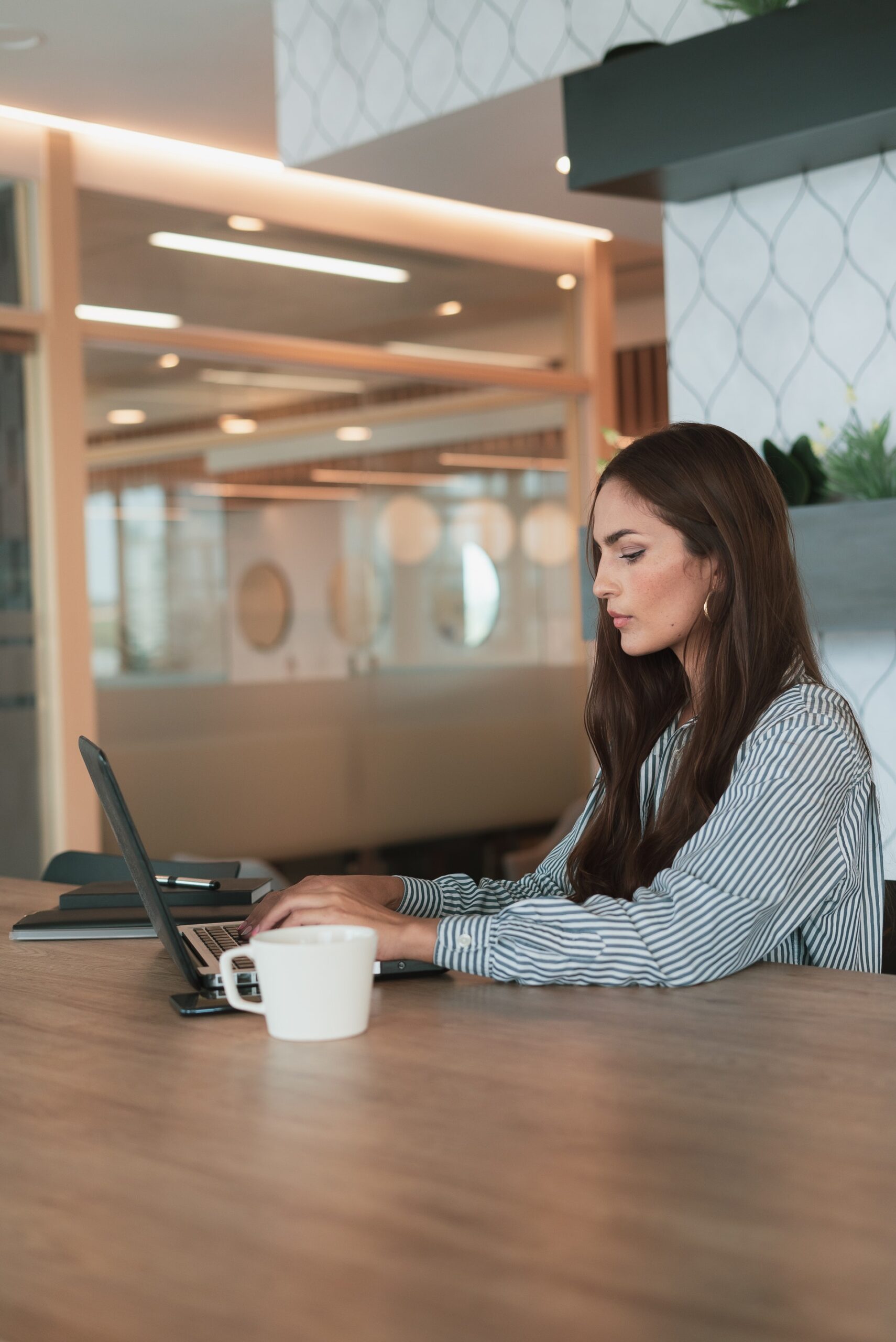 Femme blanche aux cheveux châtains assise à une table de réunion travaille sur son ordinateur portable