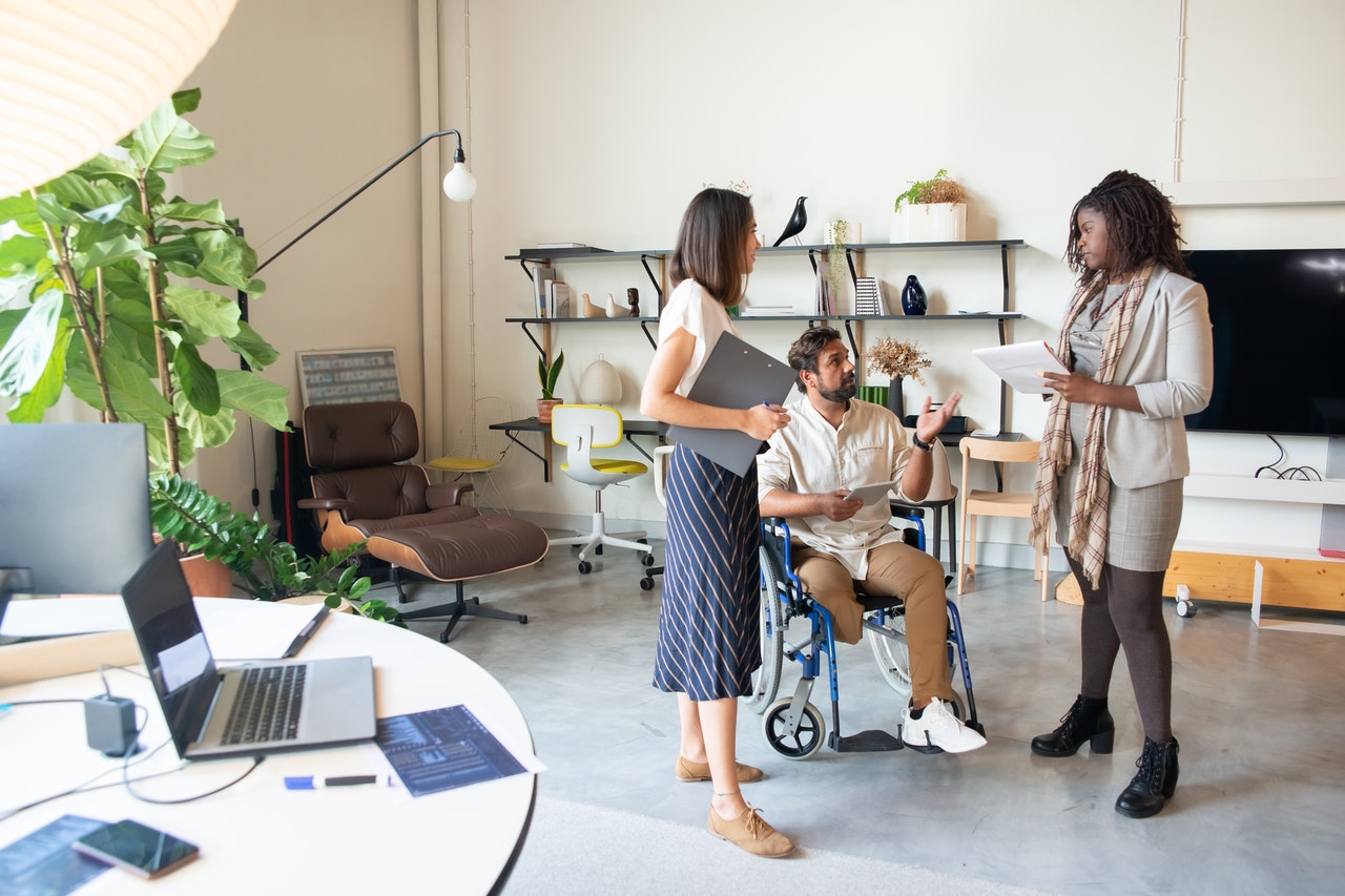 Un homme en fauteuil roulant parle à deux femmes debout dans un bureau