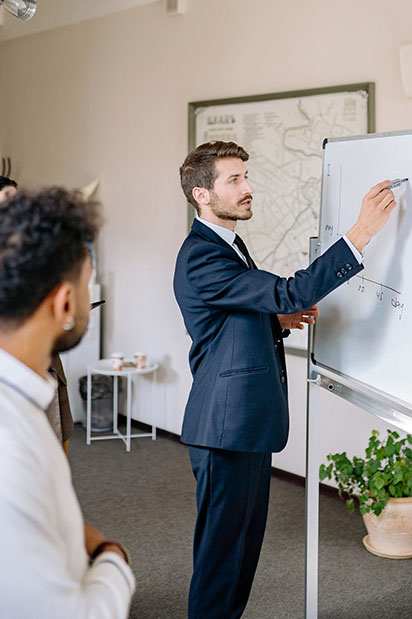 Un homme blanc écrit sur un tableau blanc