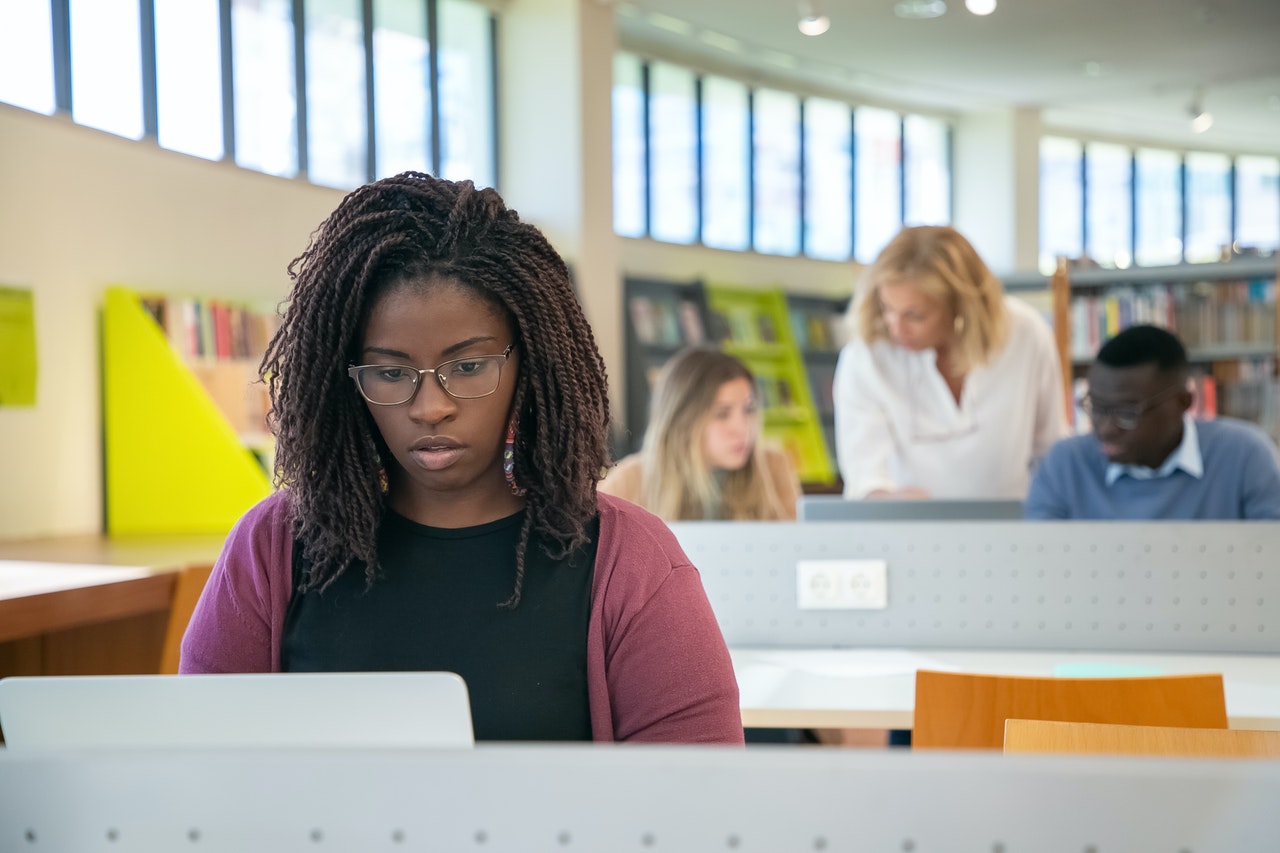 Une étudiante noire assise devant un ordinateur dans une bibliothèque