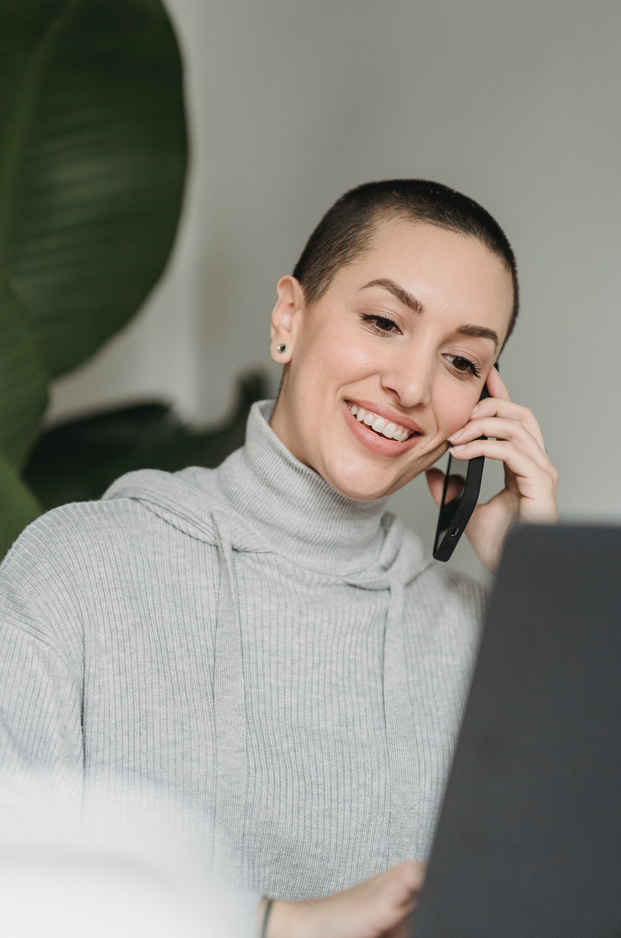 Femme blanche aux cheveux rasés souriante au téléphone