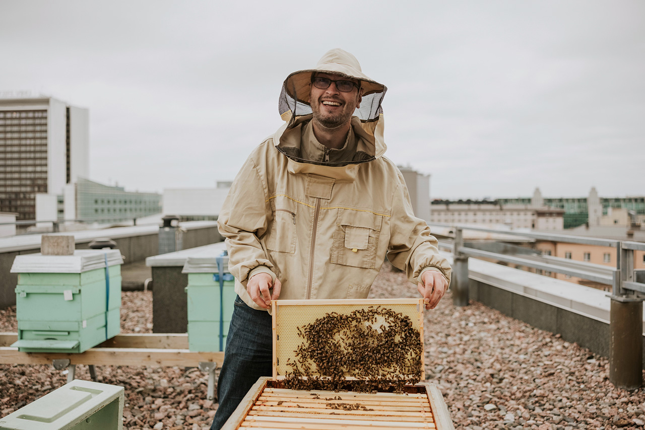 Un homme en tenue d'apiculteur soulève un rayon d'une ruchesur un toit