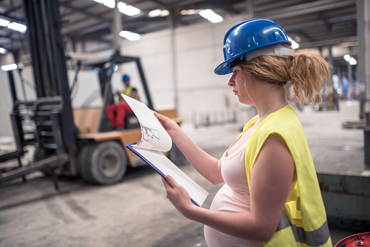 Femme blanche enceinte avec un casque de protection dans une usine