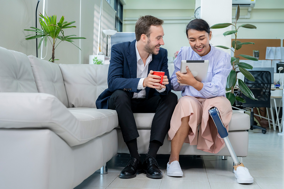 Un homme blanc et une femme asiatique avec une prothèse de jambe assis sur un canapé en entreprise