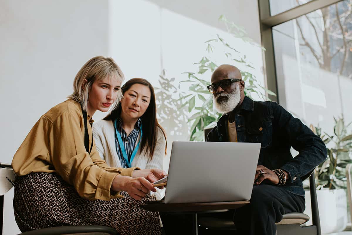 Homme noir à la barbe blanche une femme asiatique et une femme blanche assis devant un ordinateur