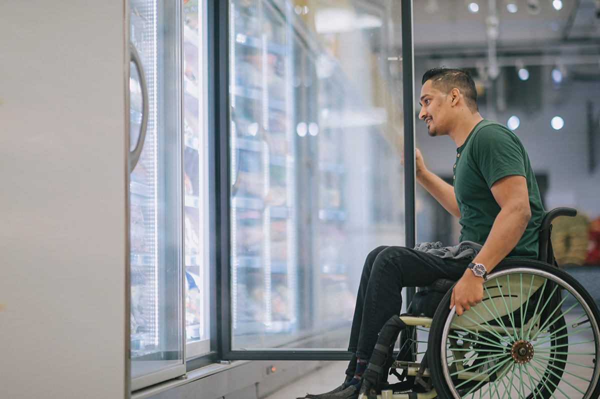 Homme asiatique en fauteuil roulant ouvre la porte d'un réfrigérateur dans un magasin