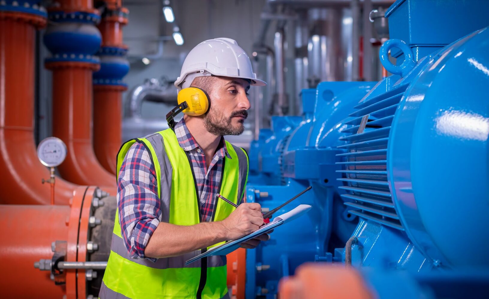 Homme en gilet jaune et casque blanc, observe une pompe dans une usine et prend des notes sur un document
